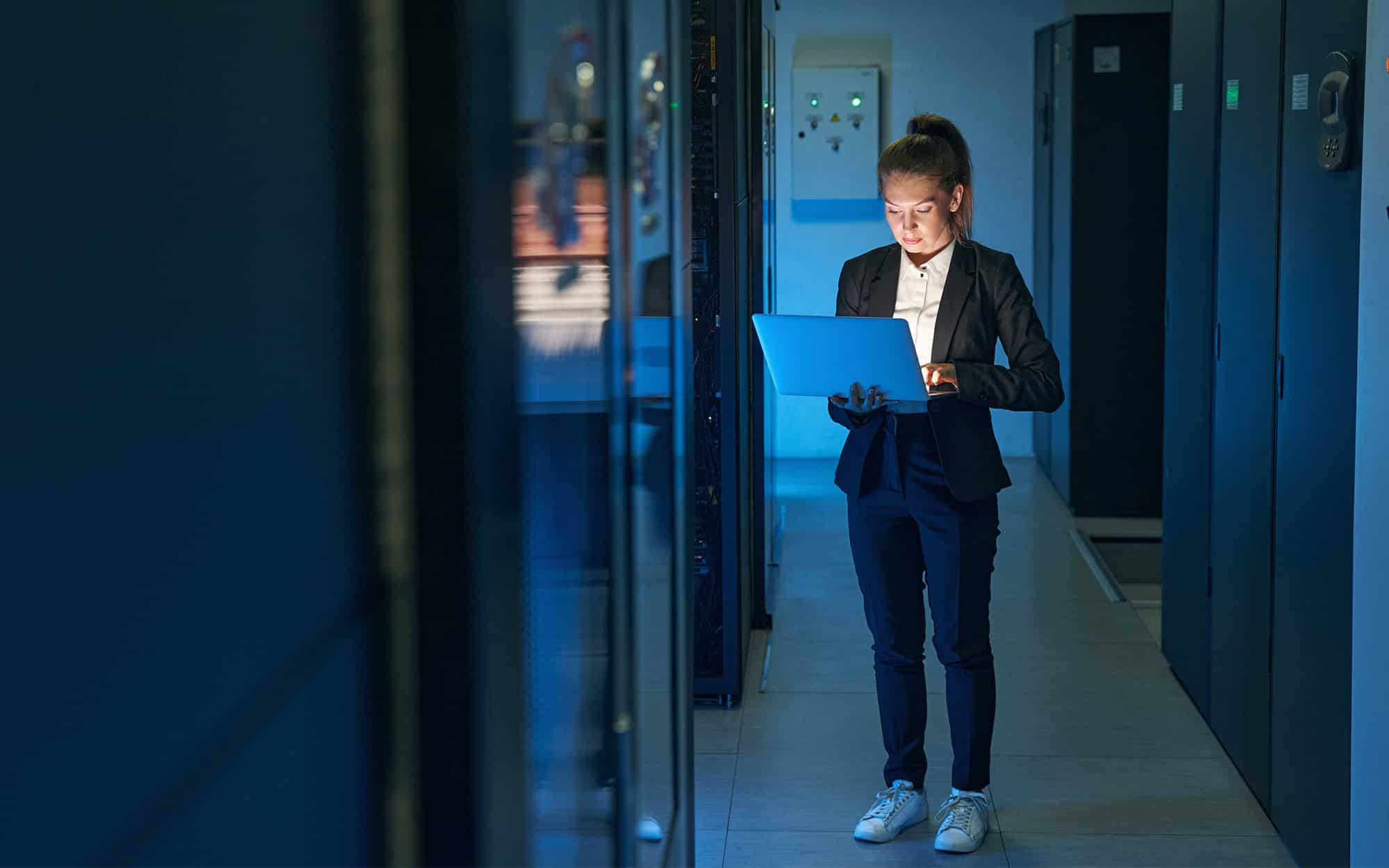 Technician in Server Room Analyzing Data on Laptop