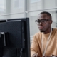 Front view of a man in an orange sweater looking at a computer monitor